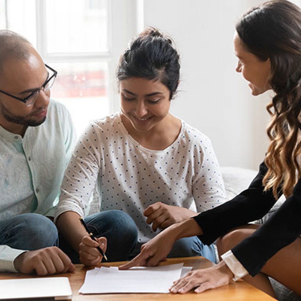 Happy diverse couple satisfied clients making deal, Indian wife signing contract at meeting after successful negotiation with realtor, mortgage insurance broker, family purchasing new apartment